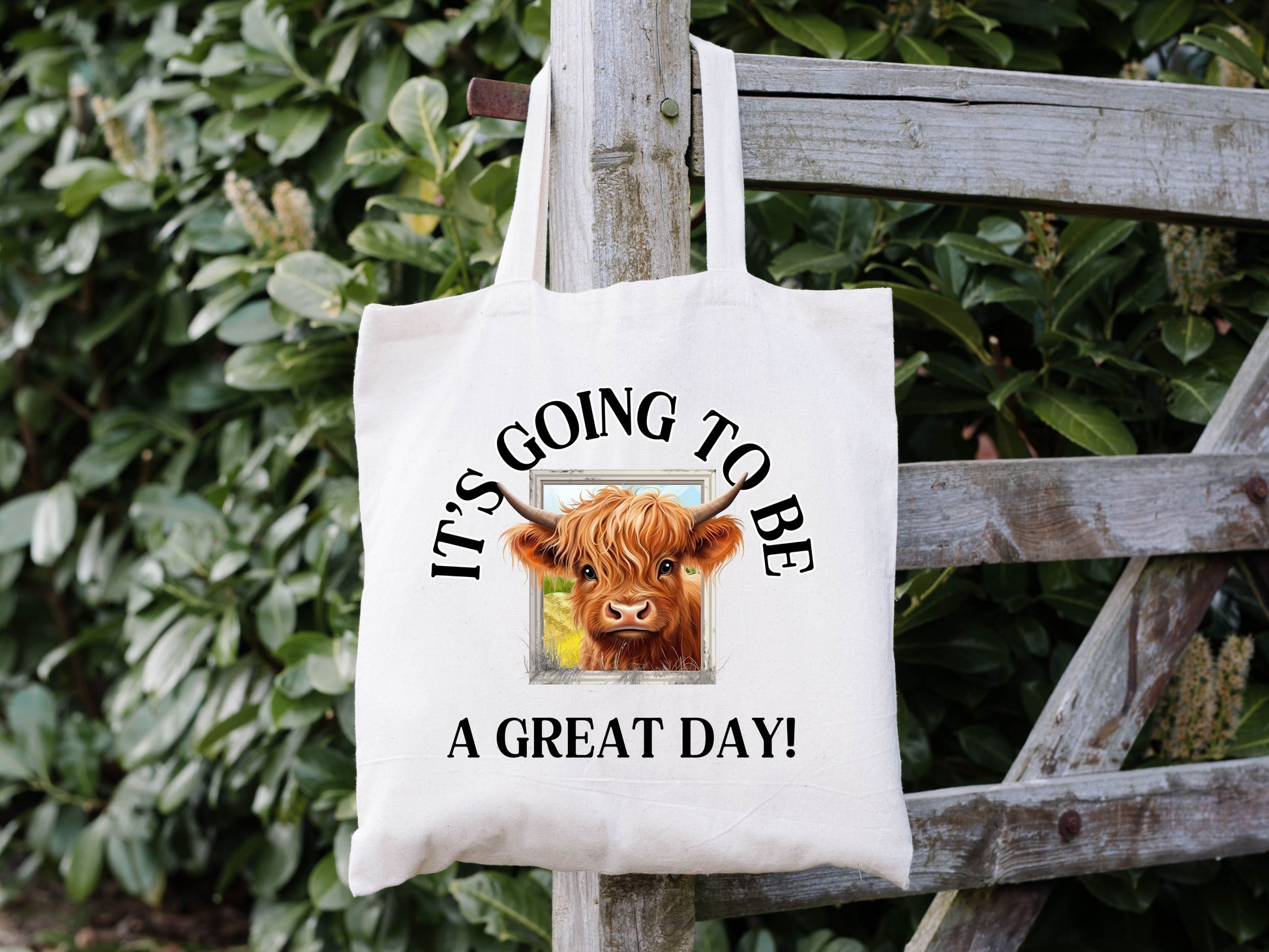 white tote bag with an image of a highland cow sticking it's head out of a window. around it says "it's going to be a great day!"