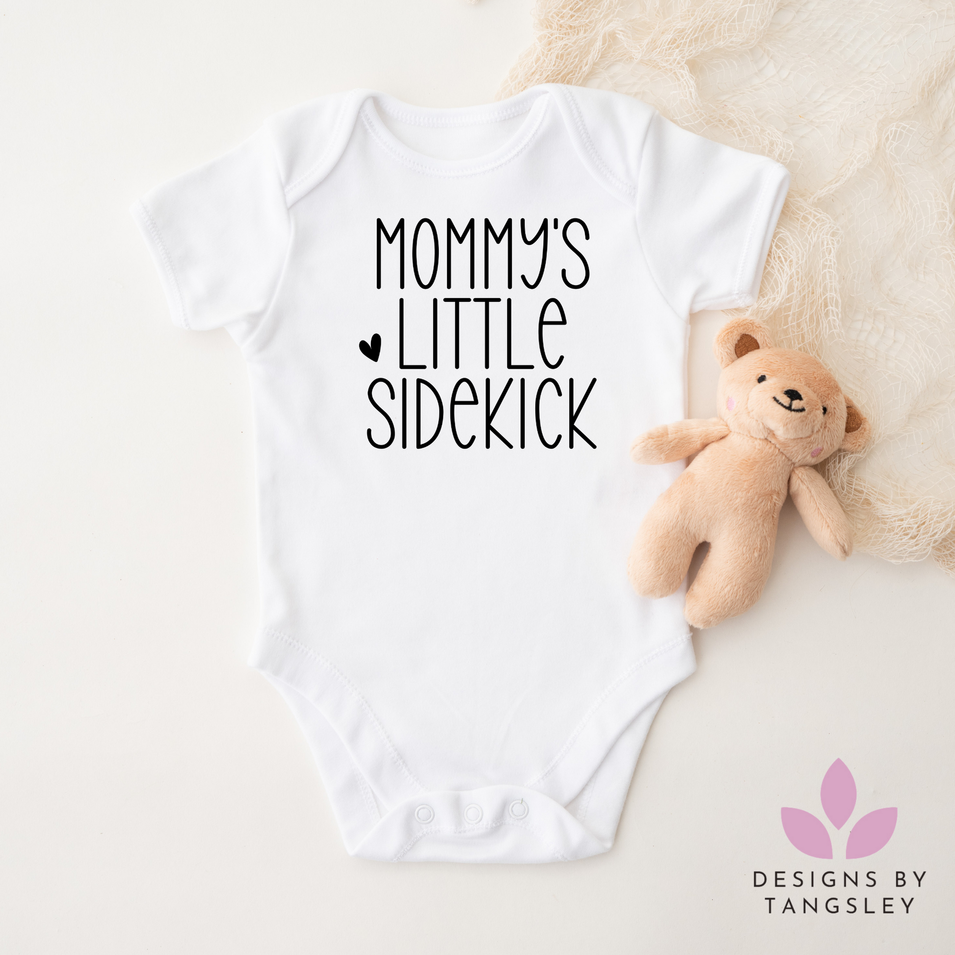 White shortsleeved bodysuit that says mommy's little sidekick with a small heart in black.