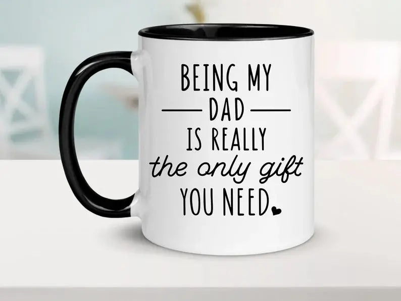 White coffee mug with black handle and black inside. It says "being my dad is really the only gift you need" with a small heart as the period.