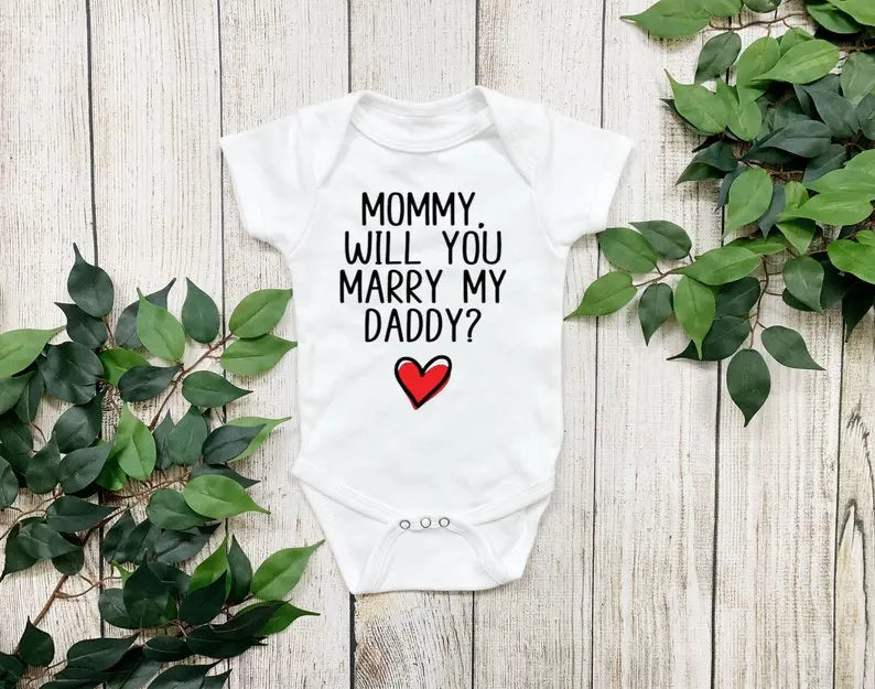 White short sleeved bodysuit that says MOMMY WILL YOU MARRY MY DADDY? in a black font and there's a red and black heart below it.
