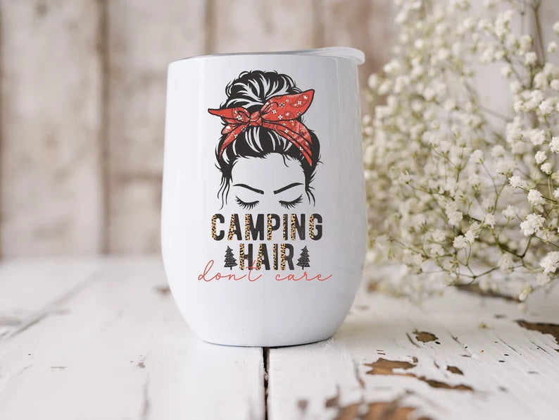 White wine glass tumbler with lid. It has an image of a girl with a messy bun and it says camping hair don't care. with cheetah print accents.