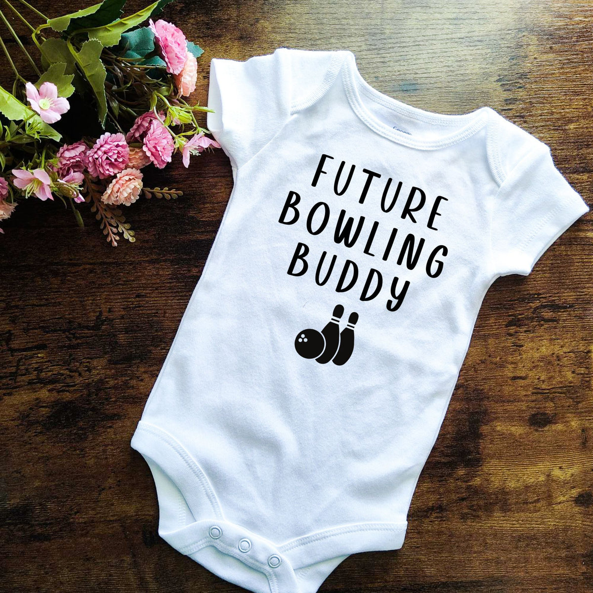 White short sleeved baby bodysuit with a black design that says FUTURE BOWLING BUDDY with an image of a bowling ball and two pins.