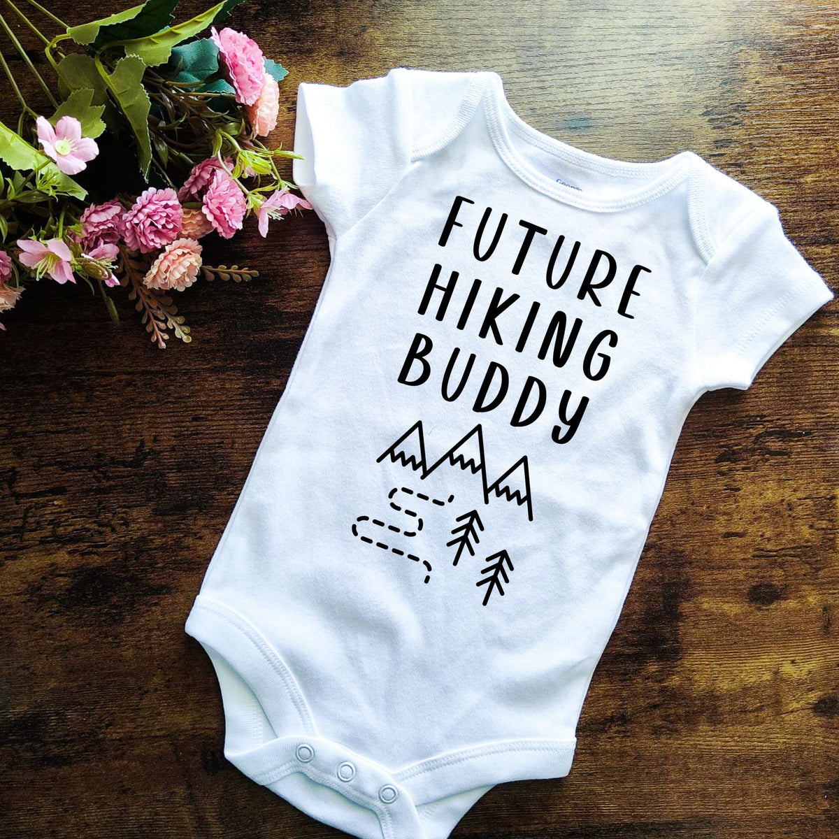 white short sleeve baby bodysuit that says FUTURE HIKING BUDDY with simple design of mountains and a trail in a wooded area