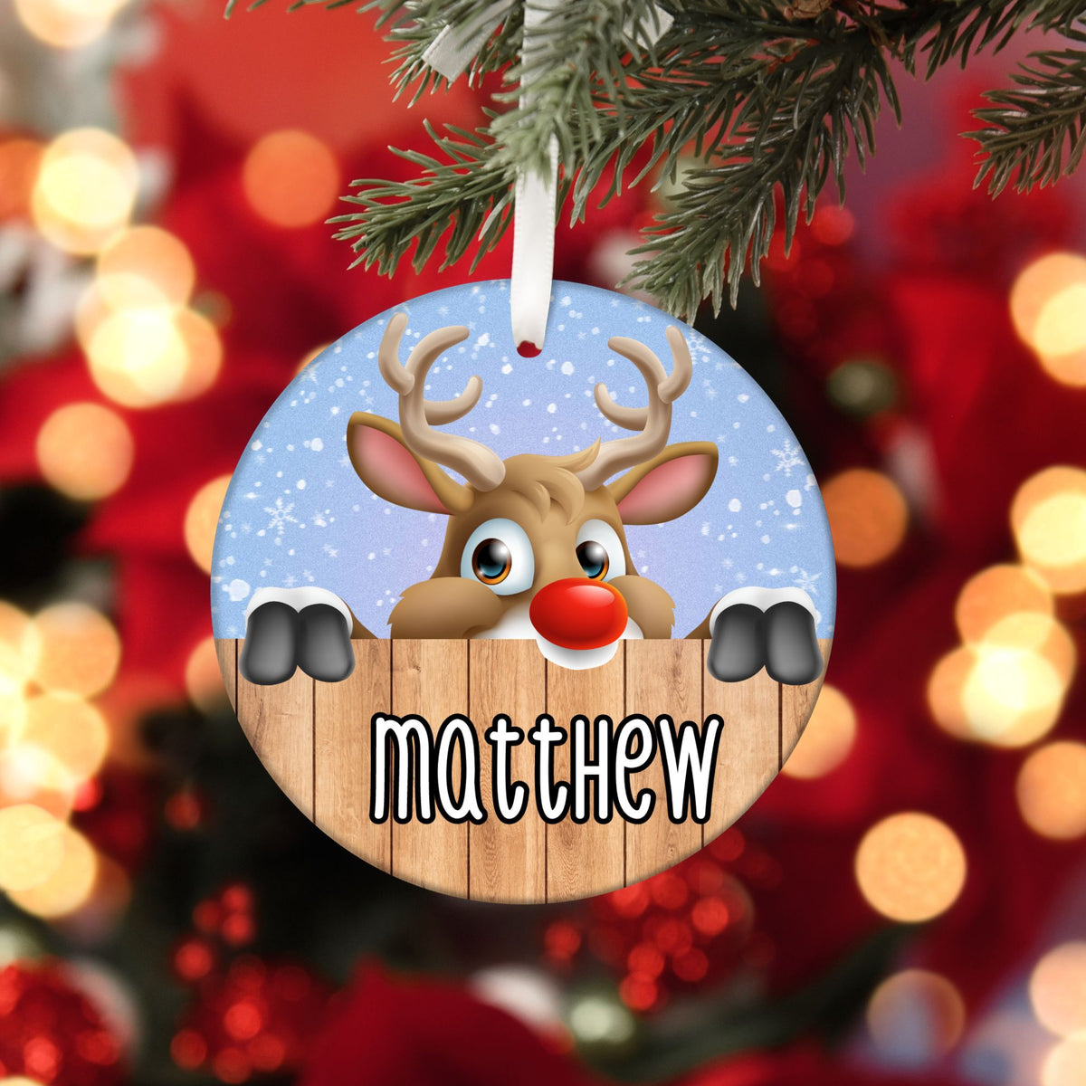 Round ornament with white ribbon. It has the name "matthew" on it with a cute reindeer peaking over a fence.