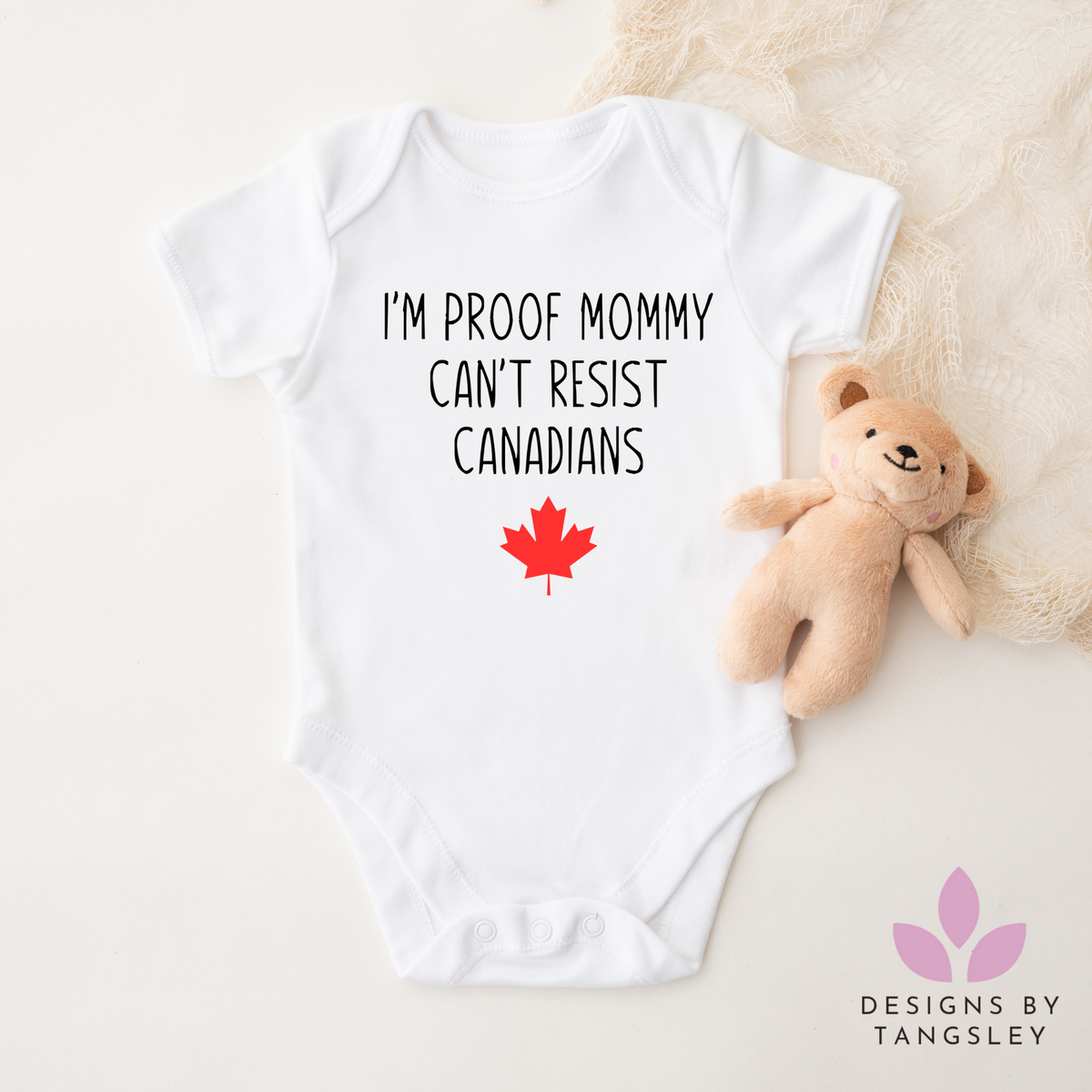 Shortsleeve white baby bodysuit that says I'M PROOF MOMMY CAN'T RESIST CANADIANS in black with a red maple leaf in red. Made by Designs by Tangsley