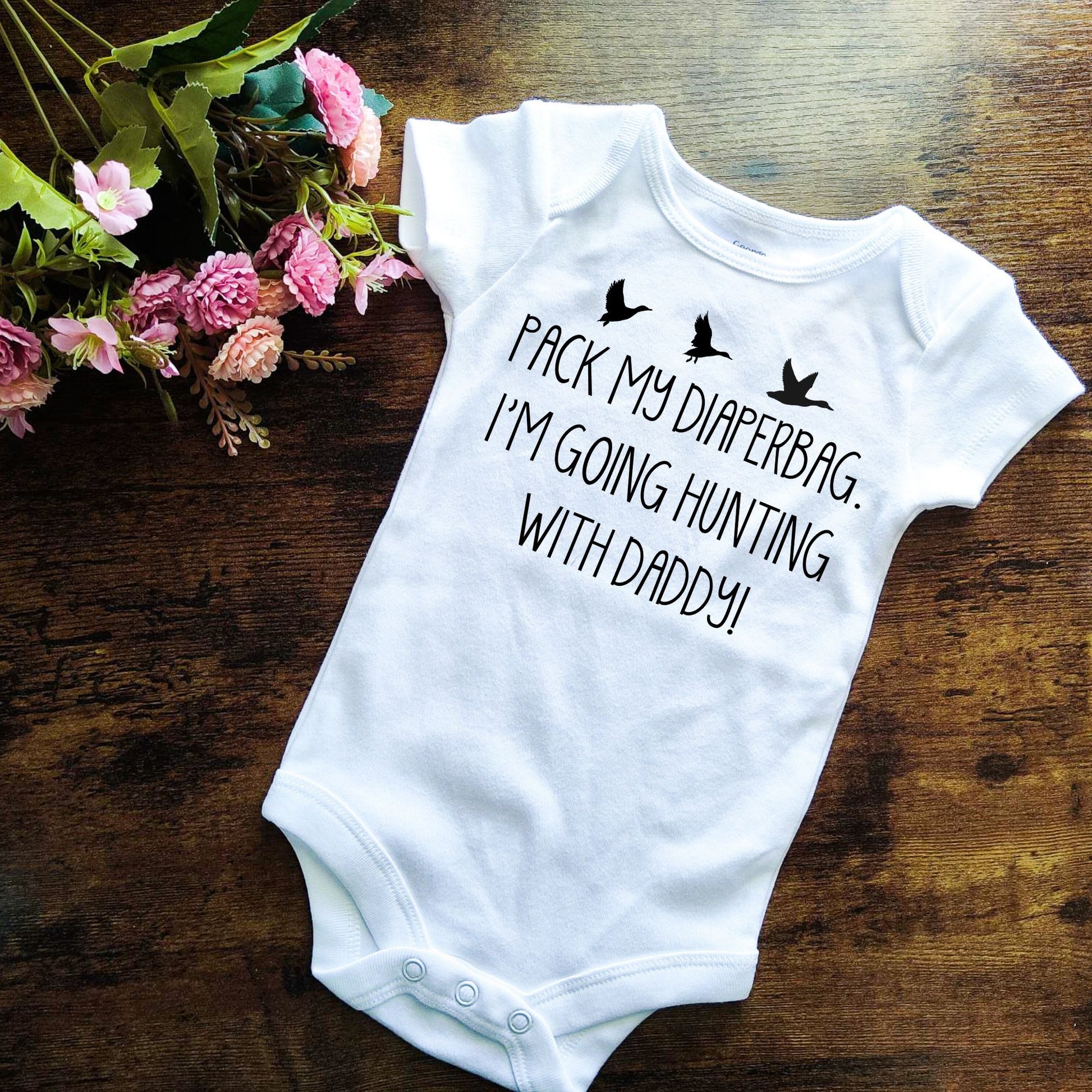 White bodysuit with black design. It shows birds flying and it says "PACK MY DIAPERBAG. I'M GOING HUNTING WITH DADDY!"