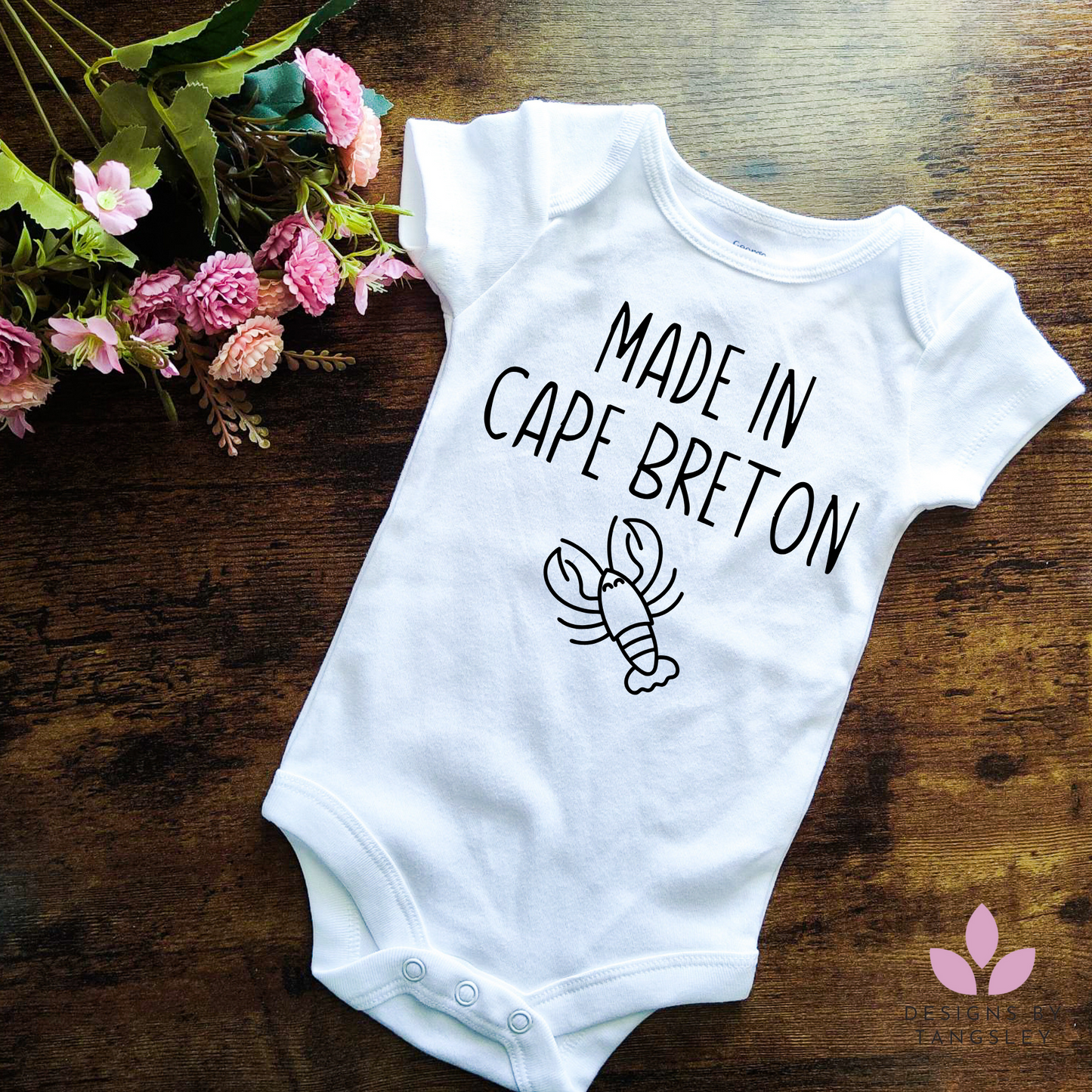 baby bodysuit. white in color with black design that says MADE IN CAPE BRETON with a little lobster lineart below it.