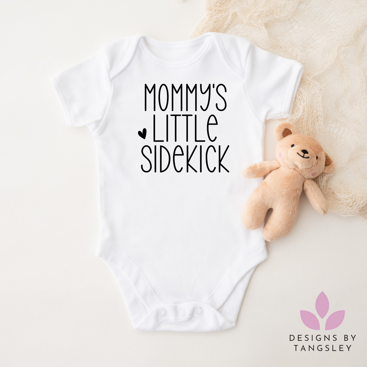 White shortsleeved bodysuit that says mommy's little sidekick with a small heart in black.