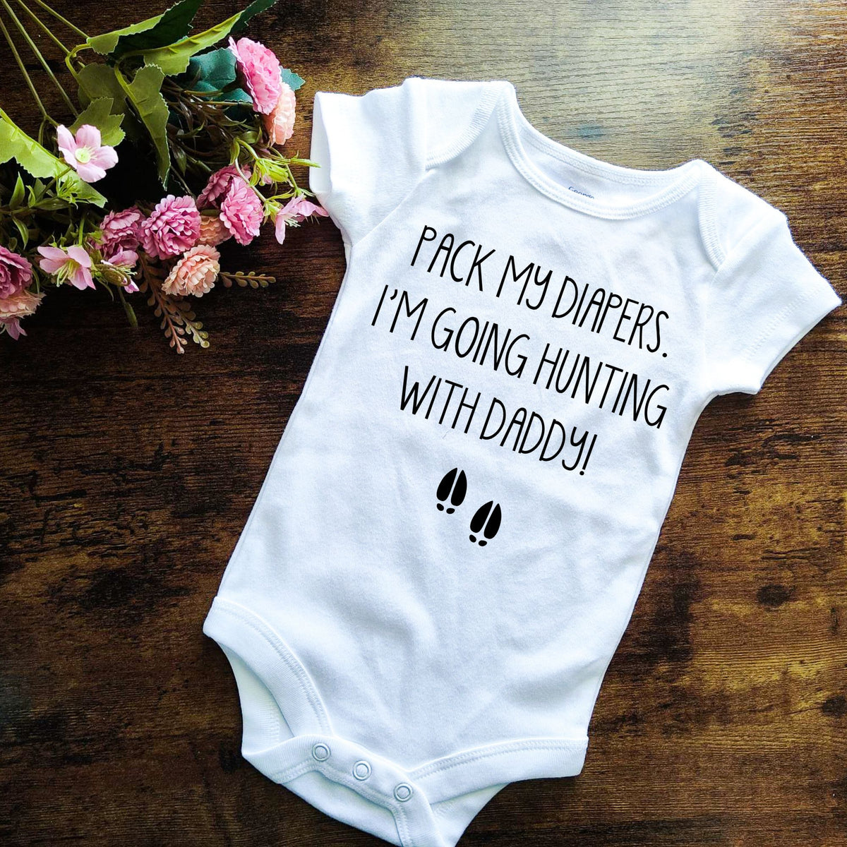 White baby bodysuit with the phrase “Pack my diapers. I’m going hunting with Daddy!” in black text, featuring small deer hoof prints; handmade in Cape Breton, Nova Scotia.