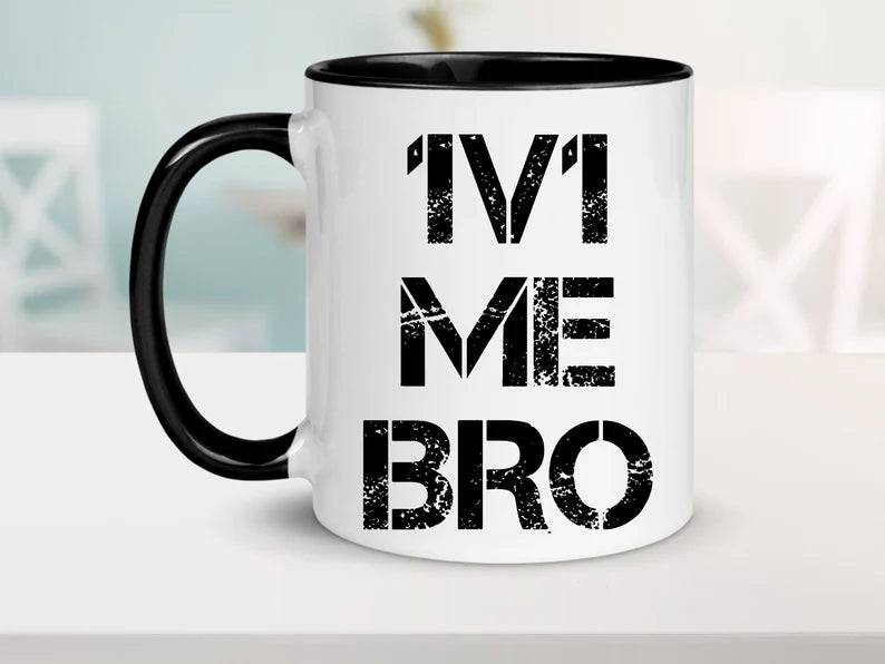 White coffee mug with black handle and black inside. It says "1v1 ME BRO" in a faded masculine font