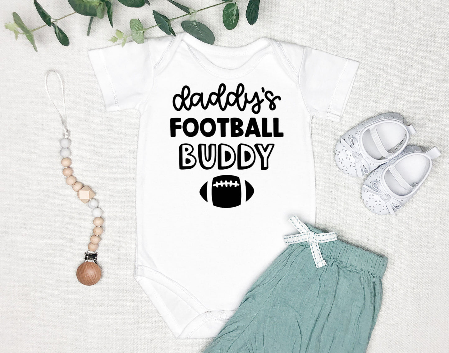 White short sleeved baby bodysuit that says daddy's football buddy with an image of a football below it.