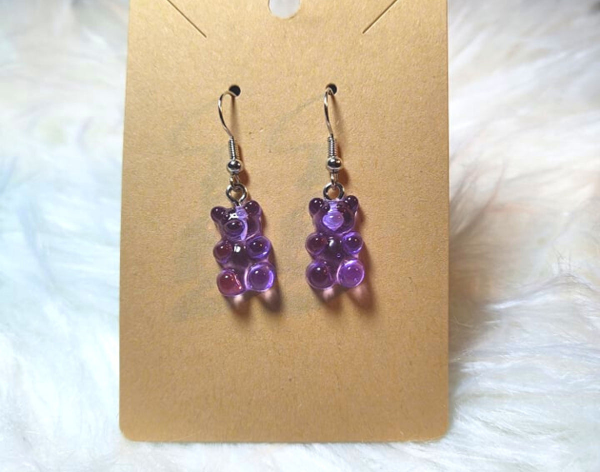 An earring card with dangle bear earrings. Silver metal components and the bears are a transparent purple color. 