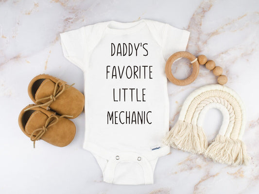 white short sleeved bodysuit for babies. The design is in black and says "daddy's favorite little mechanic"