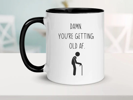 White and black coffee mug with a saying "damn. you're getting old af." with a picture of a stick figure with a cane
