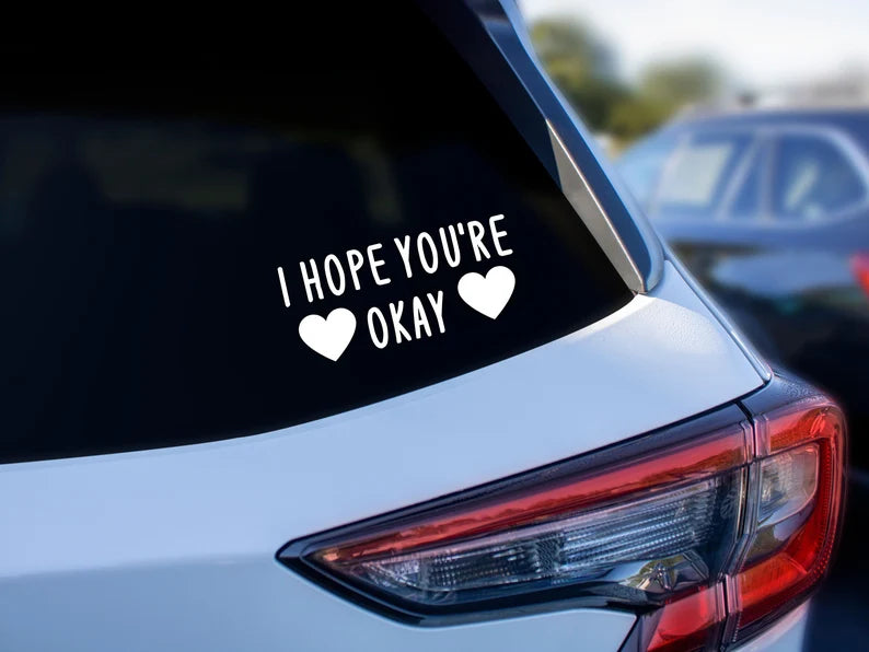 The back of a car. On the window it says "I HOPE YOU'RE OKAY". with two hearts around "okay".